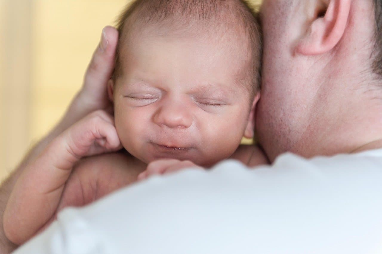 Un bebé recién nacido dormido sobre el hombro de su papá