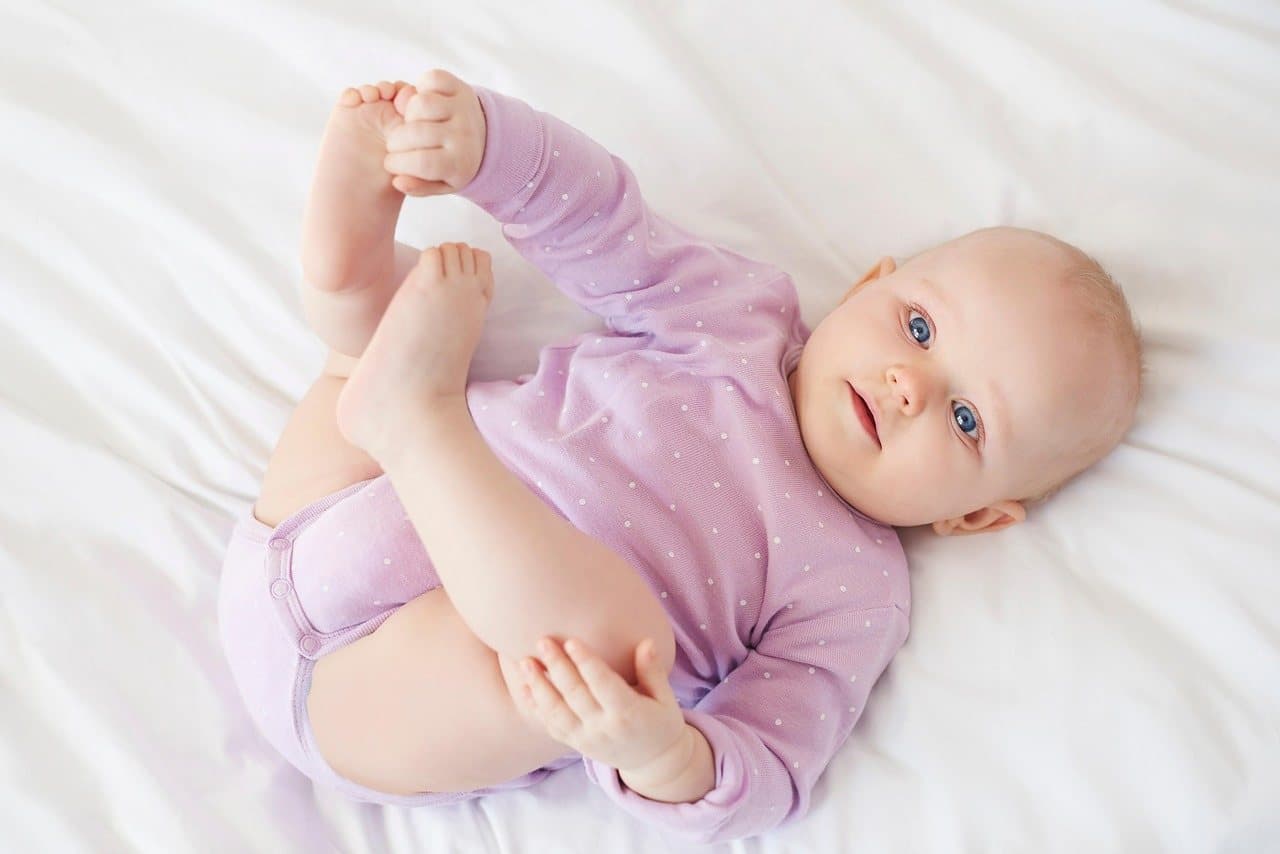 Una beba de cuatro meses acostada, agarrándose los pies