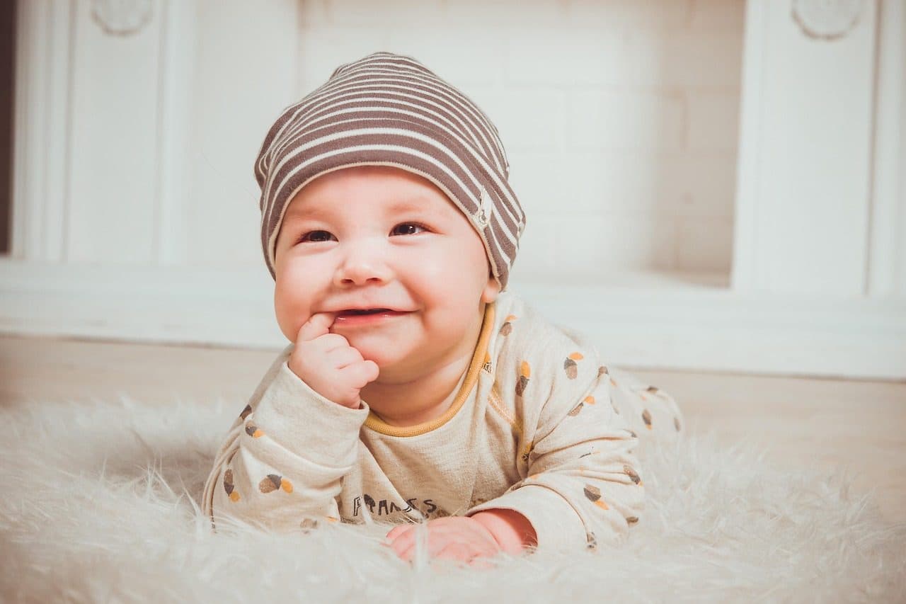 Un bebé boca abajo sobre una alfombra, sonriendo con un gorro a rayas