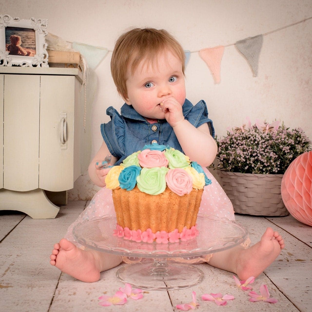 Una beba de un año sentada en el piso, comiendo de una torta con flores de crema